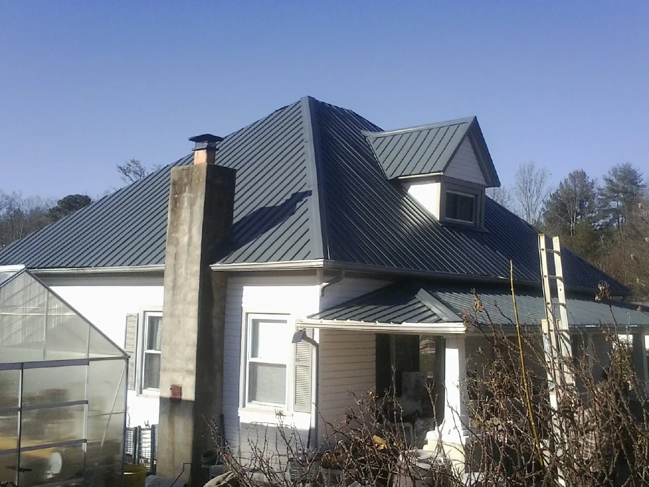 Dark blue standing seam metal roof on a white farmhouse with dormer — Slate & Tile Roof Repair by Roofing Brothers in Avalon