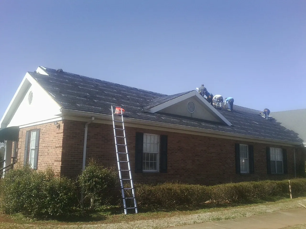 Crew tearing shingles off a brick ranch roof with a ladder set — Emergency Roof Repair work by our crew in Avalon