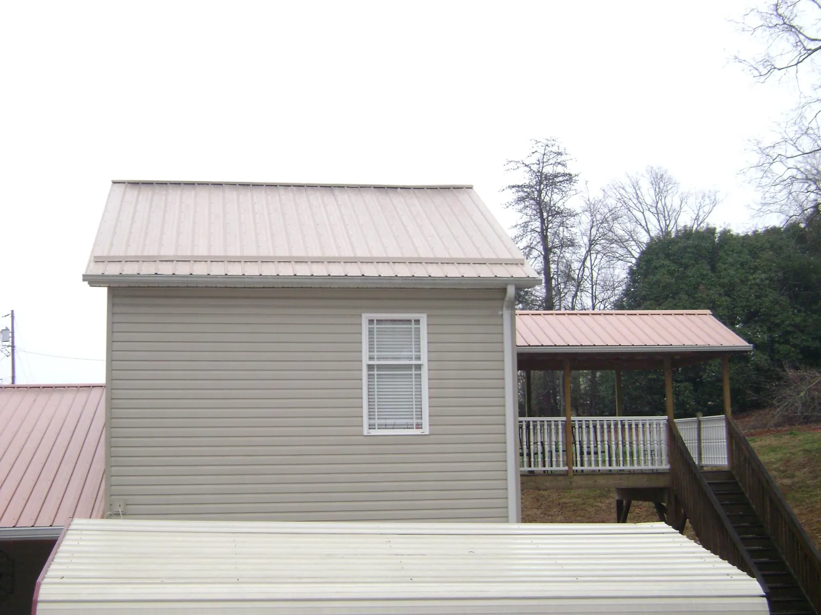 Tan metal roofs on a two story addition and attached porch, from a Roof Replacement job in Avalon